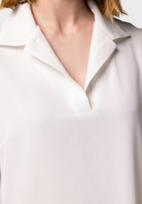 Blusa bianca con scollatura a V profonda e colletto a risvolto. Tessuto liscio, leggero e design minimalista senza decorazioni.