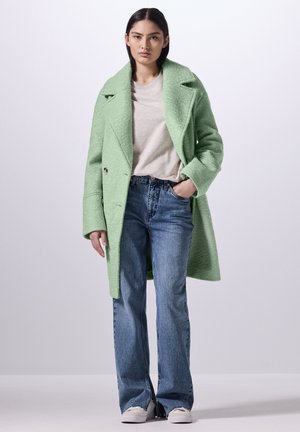Mint green, textured wool coat with oversized collar, single-breasted closure, paired with light blue, flared denim jeans and white sneakers.