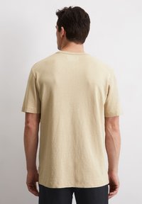 Beiger T-Shirt mit kurzen Ärmeln aus weichem Stoff, mit einem Rundhalsausschnitt und einer leicht lockeren Passform. Einfaches Design mit minimalen Akzenten.