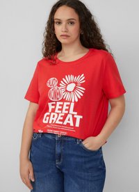 Czerwona bawełniana koszulka z krótkim rękawem, ozdobiona białym napisem i grafiką kwiatów. Okrągły dekolt, luźny krój. W zestawieniu z niebieskimi dżinsami.