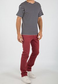 Striped navy and cream t-shirt, round neckline, short sleeves, paired with red slim-fit jeans and white sneakers. Focus on casual outfit style.