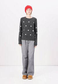Gray sweater with white heart patterns, paired with gray wide-leg jeans and brown shoes. Model wears a red knitted beanie.