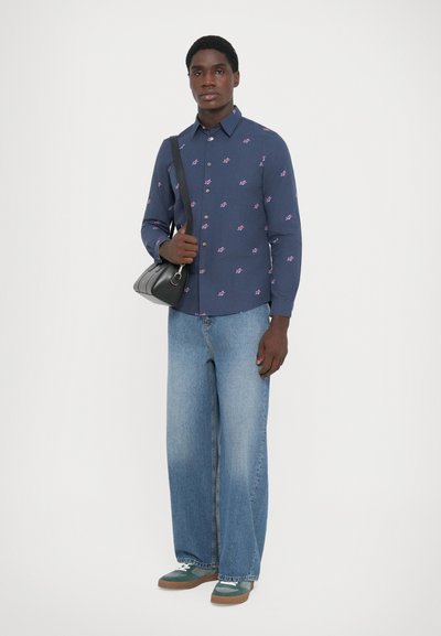 Marineblå skjorte med rosa blomsterprint, kombinert med vide lyseblå jeans og grønne sneakers med hvite detaljer; bærer en svart veske.