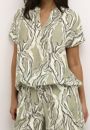 Femme portant un haut ample à manches courtes et col en V, ainsi qu'un pantalon large assorti avec un motif abstrait tourbillonnant beige et noir.