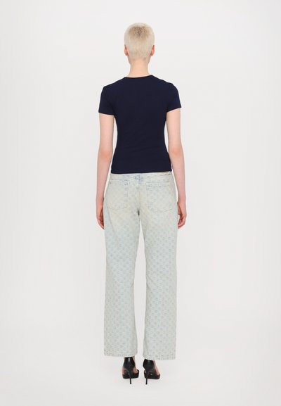 Navy fitted t-shirt, short sleeves, paired with light blue patterned wide-leg jeans. Black heeled shoes, plain background.