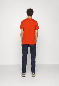 Kortärmad orange t-shirt tillsammans med marinblå cargobyxor. T-shirten har en avslappnad passform; cargobyxorna har sidofickor och en rak silhuett.