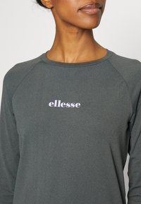 Grå långärmad skjorta med rund halsringning, med en mjuk textur och en lilafärgad "ellesse"-logotyp centrerad på bröstet.