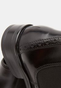 Czarny skórzany but o gładkim wykończeniu, warstwowym obcasie, przeszyciach i elastycznym bocznym panelu ułatwiającym zakładanie.