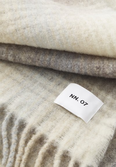 Vuneni šal u krem i sivoj boji, sa mekanom teksturom i prugastim uzorkom, završava se bijelom oznakom koja glasi "NN. 07."