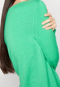 Green sweater with a soft, textured knit. Features a wide neckline and relaxed fit with dropped shoulders, showcasing a vibrant color.