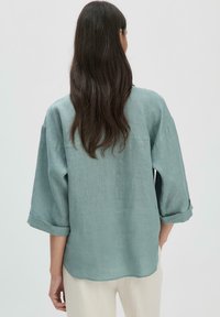 Camicia di lino azzurro chiaro con maniche a tre quarti e risvolti, caratterizzata da una vestibilità rilassata e una leggera texture. Vista posteriore mostrata.
