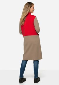 Cardigan lungo con una parte superiore rossa e una parte inferiore beige. Realizzato in un materiale a maglia testurizzato con una vestibilità dritta e spacchi laterali.