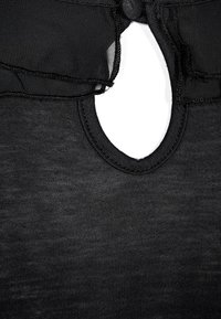 Svart topp med en rund öppning bak, tillverkad av ett mjukt, texturerat tyg med råa kanter. Snörning i nacken för justering.