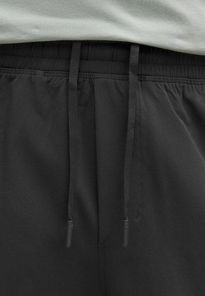 Shorts de sport noirs avec une taille élastique et un cordon de serrage. Fabriqués en tissu lisse, ils comportent des poches latérales et un design épuré.