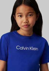 T-shirt in cotone blu reale con logo bianco "Calvin Klein" sul davanti, collo rotondo classico e maniche corte.