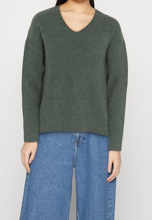Maglione a coste di colore verde scuro con scollo a V e maniche lunghe, abbinato a jeans in denim a gamba larga a vita alta. Tessuto morbido, vestibilità rilassata.