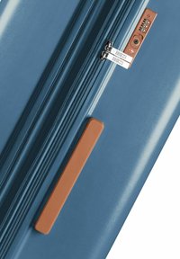 Maleta rígida azul que presenta cierres de cremallera plateados dobles, un acento de manija de plástico marrón y una cerradura de combinación incorporada con dígitos.