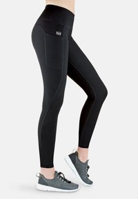 Schwarze Leggings mit hohem Bund, die nahtlose Seiten und eine Seitentasche bieten. Kombiniert mit grauen Sportschuhen mit strukturiertem Obermaterial.