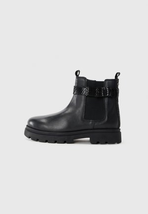 Black leather ankle boot with elastic side panels, textured black strap, and chunky rubber sole. Features pull tab for easy wear.