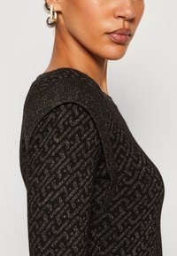 Maglione nero con un design testurizzato e accenti luccicanti, cuciture sulle spalle dettagliate e silhouette aderente.