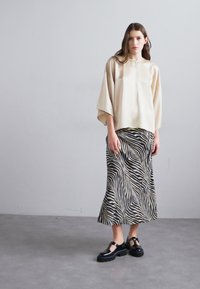 Crèmekleurige satijnen top met een ronde kraag en volumineuze mouwen, gecombineerd met een zwart-wit gestreepte rok. Zwarte chunky schoenen ronden de outfit af.