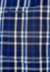 Camicia a quadri blu con motivi a scacchi blu scuro e bianco, taschino al petto e logo ricamato con filo scuro. Tessuto di cotone, texture liscia.