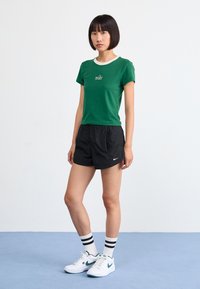 Žalias medvilninis marškinėliai su balta apykakle, juodi šortai ir balti sportbačiai. Marškinėliai ir batai turi Nike logotipą; dryžuotos kojinės.