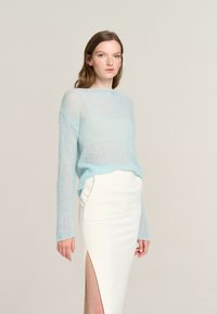 Light blue, sheer knit sweater with a round neckline and long sleeves, paired with a white, form-fitting skirt featuring a side slit.