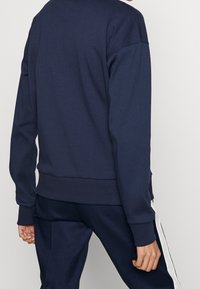 Sudadera azul marino de corte relajado, con puños y dobladillo acanalados, diseño minimalista y textura suave, combinada con pantalones a juego en azul marino.