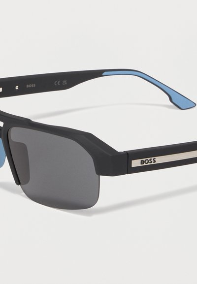 Lunettes de soleil rectangulaires noires avec des verres foncés, des branches intérieures bleues et un logo "BOSS" argenté sur la branche.
