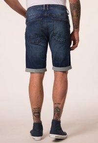 Tummansiniset farkkushortsit, joissa on käännetyt lahkeet; sisältää kaksi takataskua ja hienovaraisia ompeluyksityiskohtia; yhdistetty kankaisiin lenkkareihin.