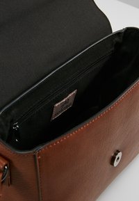 Brązowa skórzana torebka z czarnym wnętrzem. Posiada kieszeń zamykaną na suwak oraz magnetyczne zapięcie na zatrzask. Prosty, czysty design.