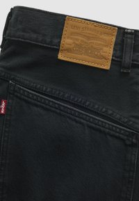 Μαύρη πίσω τσέπη τζιν Levi's με κόκκινη ετικέτα Levi's και ταμπά δερμάτινο έμβλημα της μάρκας ραμμένο στη ζώνη μέσης.