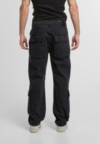 Pantaloni cargo negri cu două buzunare mari la spate, buzunare laterale și detalii cu fermoar, fabricați dintr-un material rezistent din bumbac.
