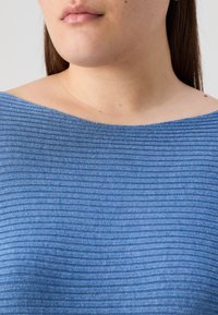 Top blu ribbed con ampia scollatura, tessuto texture con strisce orizzontali e finitura liscia. Vista ravvicinata della parte superiore del corpo.