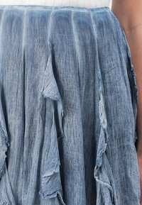 Denimblauwe rok met een gestructureerd oppervlak, voorzien van rafelige zoom en gelaagd ontwerp. Gemaakt van lichtgewicht stof met een vloeiende pasvorm.