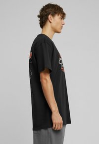 Sort bomulds T-shirt med rund halsudskæring, korte ærmer og sidetryk i rød og hvid, med en afslappet pasform.