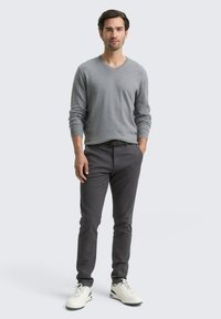 Grijze V-hals trui, donkergrijze broek en witte sneakers. De outfit heeft een casual pasvorm met textuurstof en subtiele details.