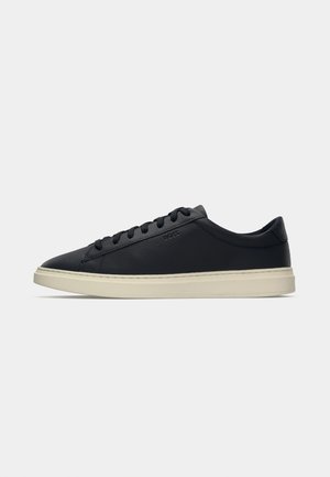 Baskets en cuir noir avec une texture lisse, profil bas, bout rond et semelle en caoutchouc crème contrastante. Caractéristiques d'un design de lacets minimaliste.