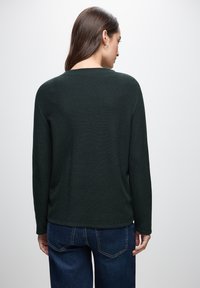 Maglione a collo alto di colore verde scuro con maniche lunghe, vestibilità comoda e texture a coste, abbinato a jeans in denim blu.