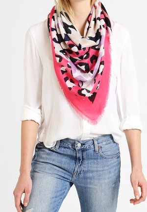 Chemise blanche à manches longues avec manches retroussées, jean bleu et foulard triangulaire à motif léopard rose, noir, violet et blanc.