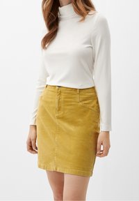 Vit långärmad turtleneck-top i kombination med en gul kordflodds-kjol, som har en framficka och en subtil struktur.