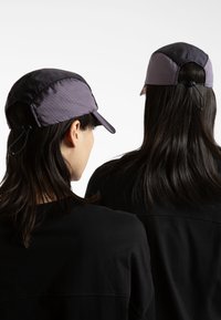 Lilla og svart justerbar cap med en strukturert skygge, laget av lett stoff med et subtilt rutemønster, båret av to personer.