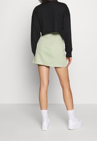 Falda verde clara en forma de A hecha de tejido suave, combinada con un top corto negro y zapatillas blancas, con una textura suave y un diseño sencillo.