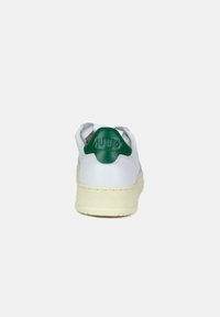 Sneaker in pelle bianca con inserto verde sul tallone, suola crema e dettagli texture. Presenta una forma tondeggiante e elementi di design minimalisti.