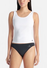 Hvit ribbestrikket tanktopp kombinert med svarte bikinibukser med tre sølvstriper på venstre side. Begge plagg har en tettsittende utforming.