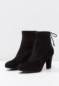 Černé kotníkové boty z broušené kůže na vysokém podpatku, s bočními výřezy, prošívanými detaily a ozdobnou mašlí na zadní straně.