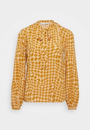 Langärmlige Bluse in Senfgelb mit einem Hahnentritt-Muster in Creme, subtiler Schleifenkragen und elastischen Bündchen an den Ärmeln.
