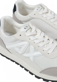 Sneakers atletiche bianche realizzate in materiali mesh e suede, con una superficie testurizzata, lacci bianchi e un accento nero sul tallone.