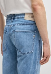 Jeans in denim blu chiaro caratterizzati da un design a gamba dritta, tasche posteriori a toppa e un'etichetta in pelle beige con il logo "BOSS" impresso sulla cintura.
